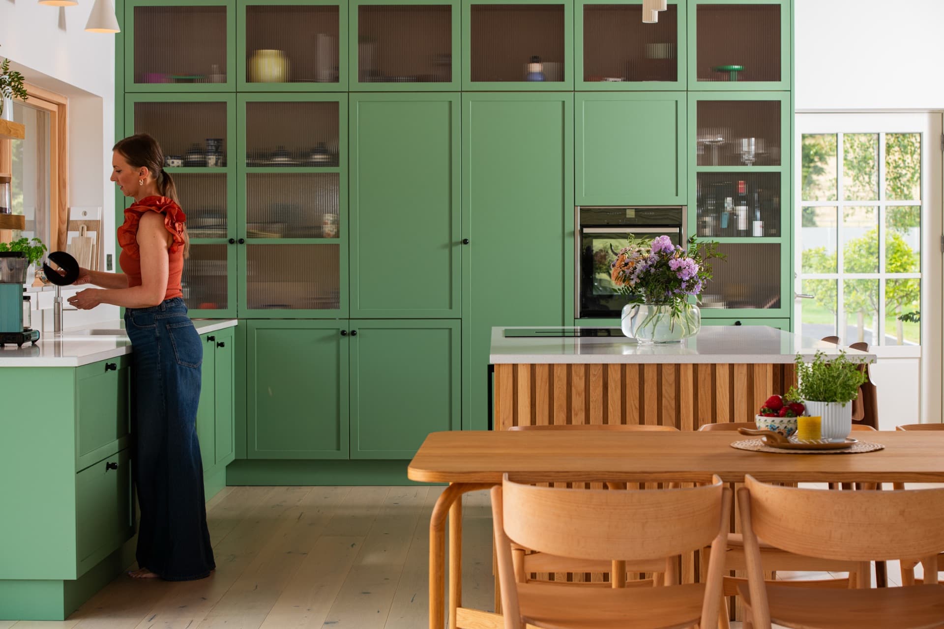 The sage-green kitchen with a long wooden table set for guests